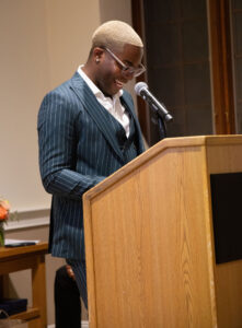 Malik stands at the podium at the 2025 Spring Gala with a proud smile as be looks down at his notes.